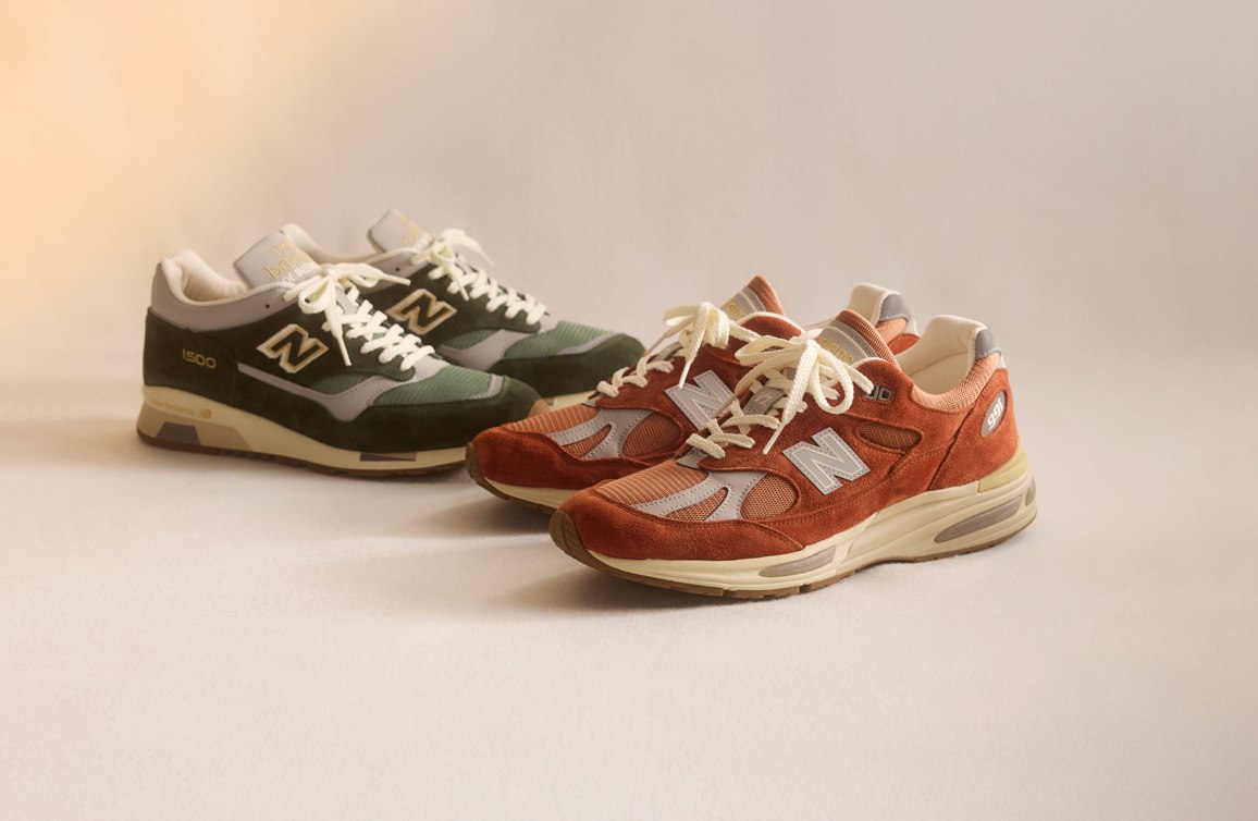Knee down view of a man and woman wearing New Balance Made in UK sneakers standing on a concrete floor against a grey wall.